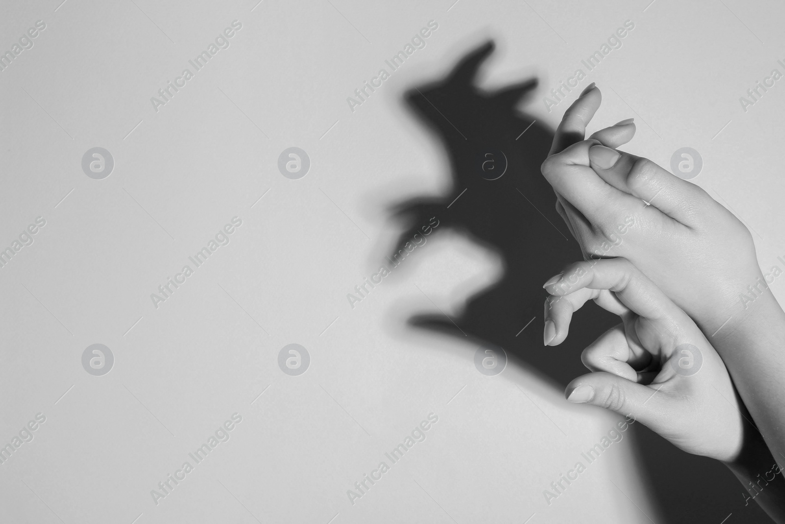 Photo of Shadow puppet. Woman making hand gesture like rabbit on light background, closeup with space for text. Black and white effect