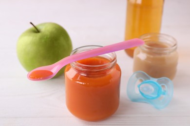 Photo of Jars with healthy baby food, bottle of juice, apple, spoon and pacifier on white wooden table