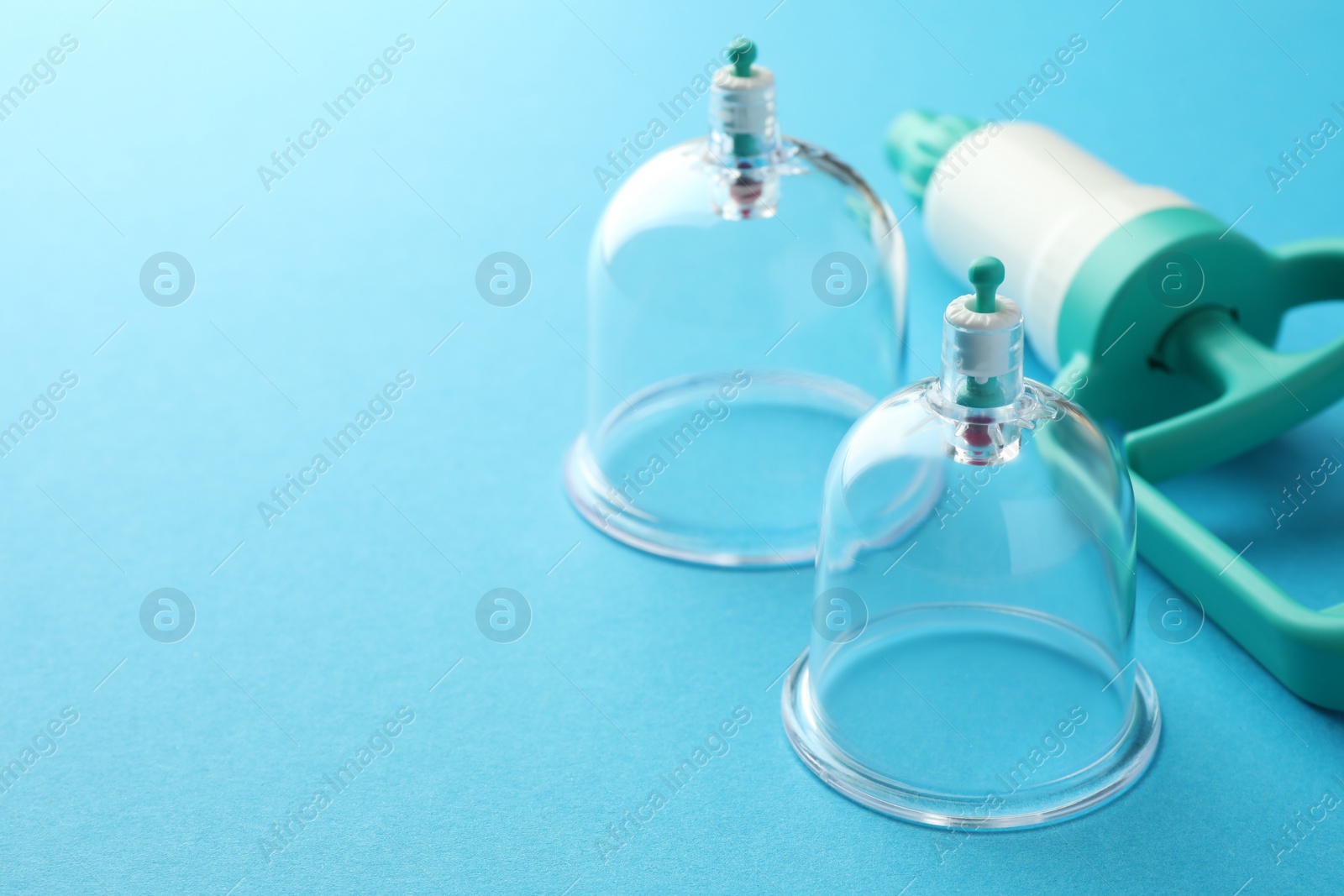 Photo of Plastic cups and hand pump on light blue background, closeup with space for text. Cupping therapy