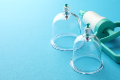 Photo of Plastic cups and hand pump on light blue background, closeup with space for text. Cupping therapy