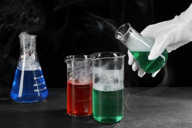 Photo of Scientist working with laboratory glassware at black table, closeup. Chemical reaction