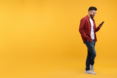 Happy young man using smartphone on yellow background, space for text