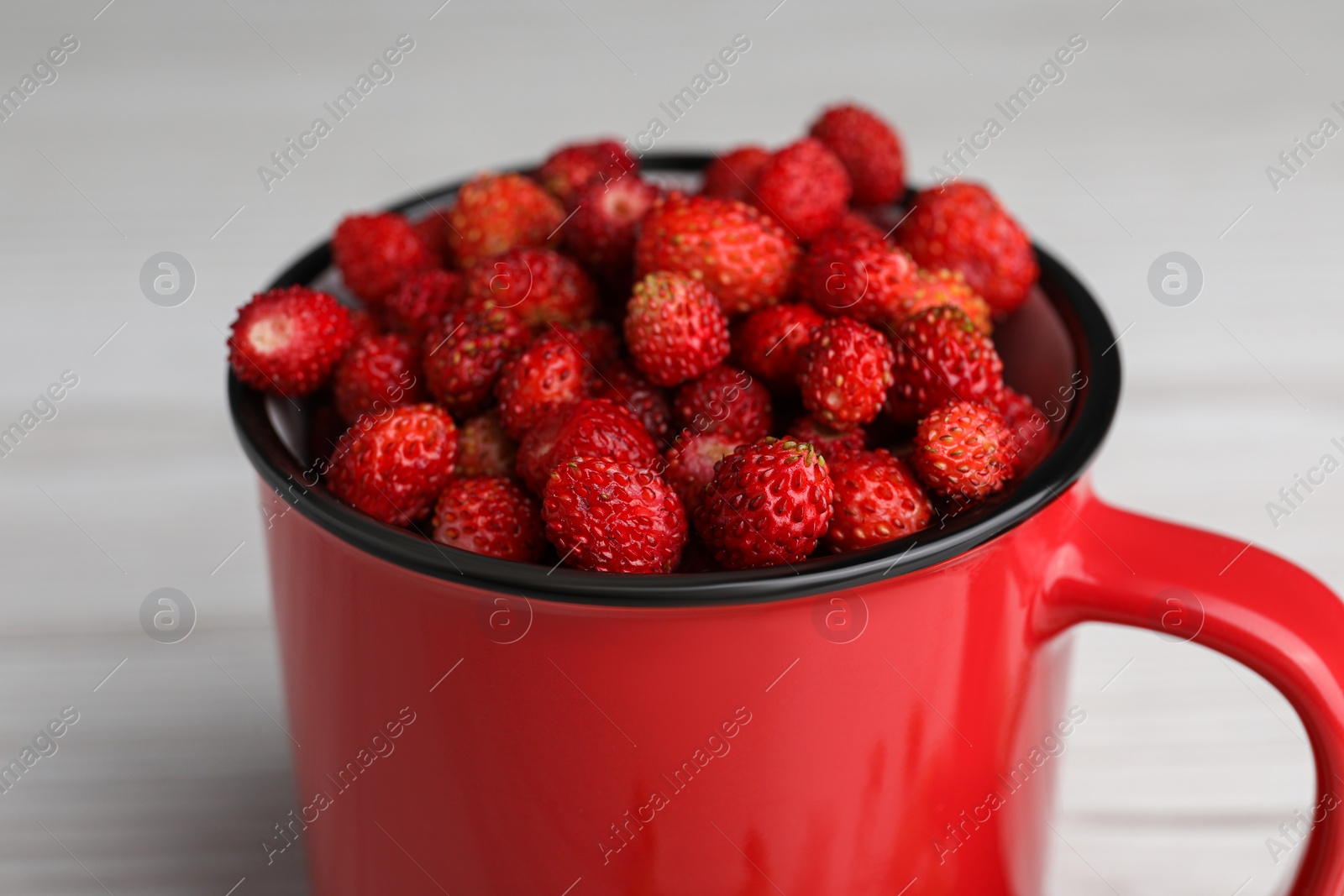 Photo of Fresh wild strawberries in mug on white table, closeup