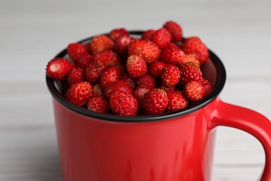 Fresh wild strawberries in mug on white table, closeup