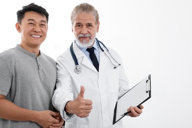 Photo of Happy doctor with clipboard making thumbs up and patient on white background. Space for text