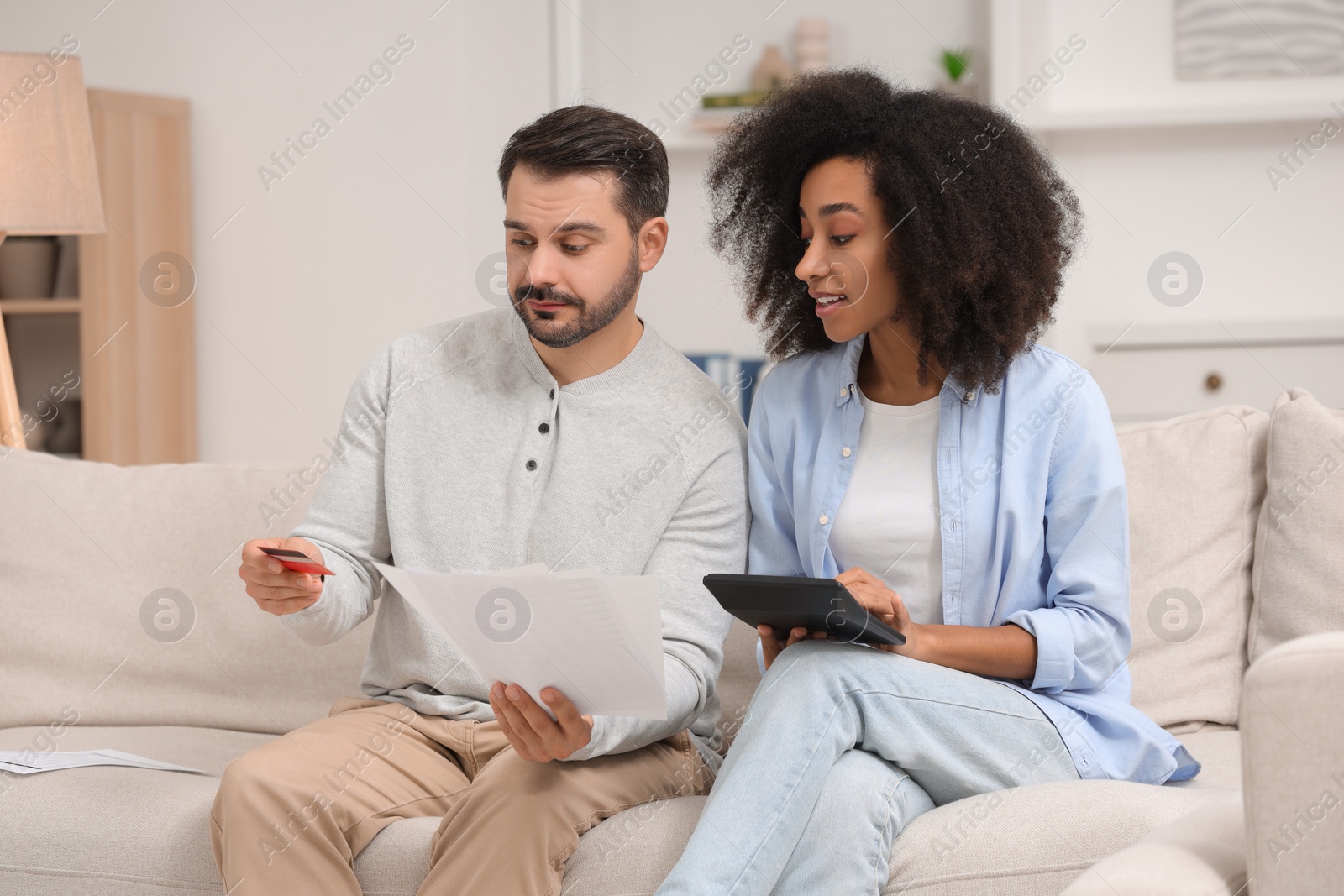 Photo of Confused couple with debt notifications, calculator and credit card planning budget at home. Financial problem