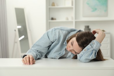 Sad young woman sitting at white table in room