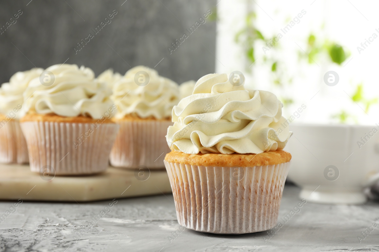 Photo of Tasty cupcakes with vanilla cream on grey table, closeup