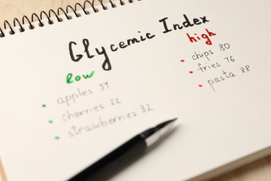 Photo of List with products of low and high glycemic index in notebook and pen on table, closeup