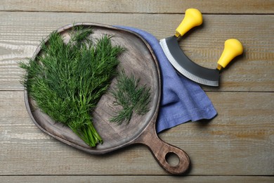 Bunch of fresh dill and mincing knife on wooden table, flat lay