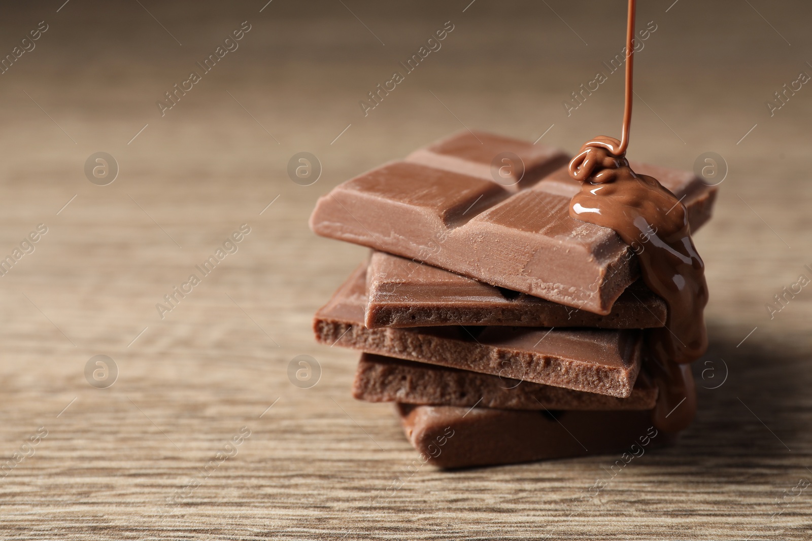 Photo of Pouring tasty milk chocolate paste onto pieces on wooden table, closeup. Space for text