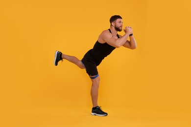Photo of Young man exercising with elastic resistance band on orange background