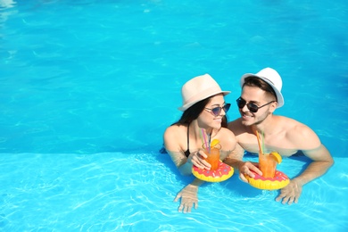 Young couple with refreshing cocktails in swimming pool on sunny day