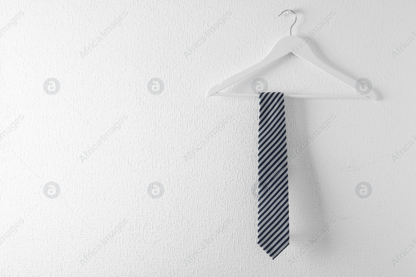 Photo of Tie on wooden hanger against white background. Space for text