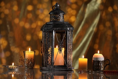 Photo of Arabic lantern and burning candles on mirror surface against blurred lights