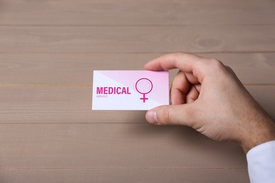 Man holding medical business card at wooden table, closeup. Women's health service