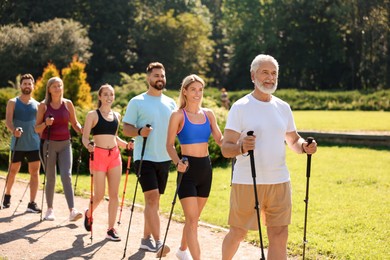 Photo of Group of people practicing Nordic walking with poles in park on sunny day