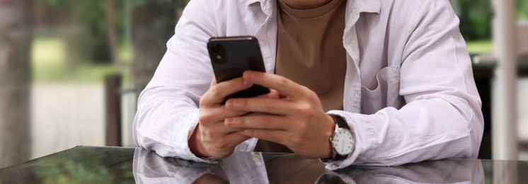 Image of Man typing message on mobile phone at table outdoors, closeup. Banner design