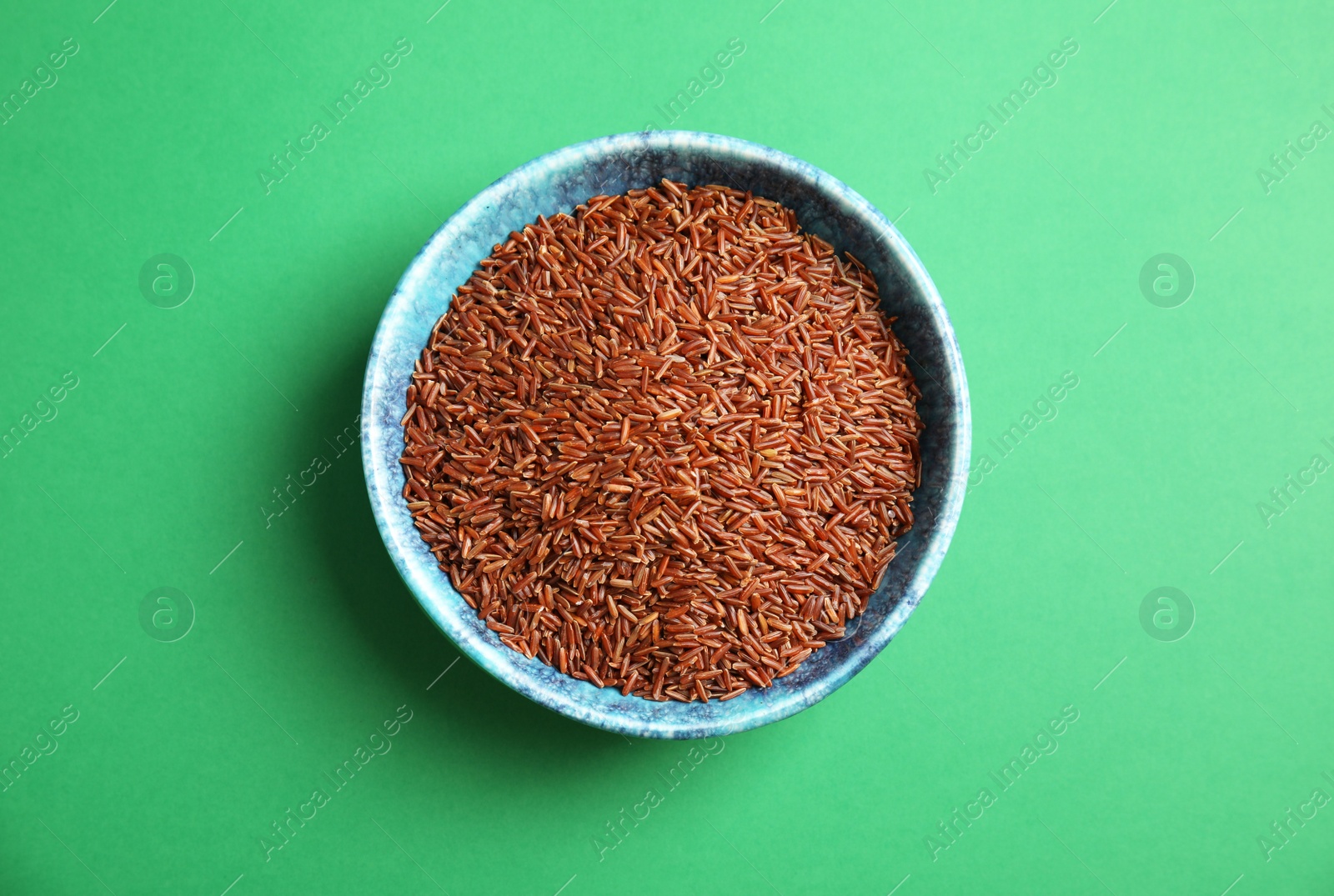 Photo of Bowl with uncooked red rice on color background, top view