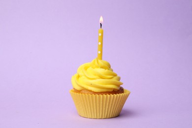Photo of Delicious birthday cupcake with yellow cream and burning candle on violet background