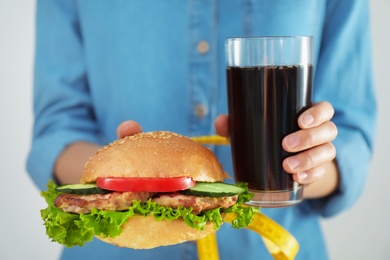 Woman with tied hands holding tasty sandwich and glass of cold drink, closeup. Healthy diet