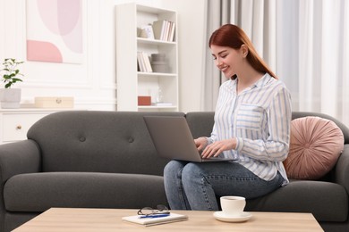 Happy woman using laptop on couch in room