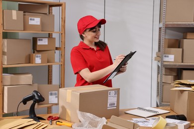 Photo of Parcel packing. Post office worker with clipboard at wooden table indoors