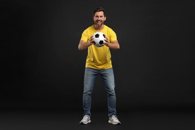 Photo of Emotional sports fan with soccer ball on black background