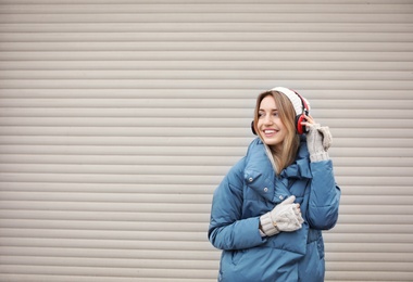 Photo of Young woman with headphones listening to music near light wall. Space for text