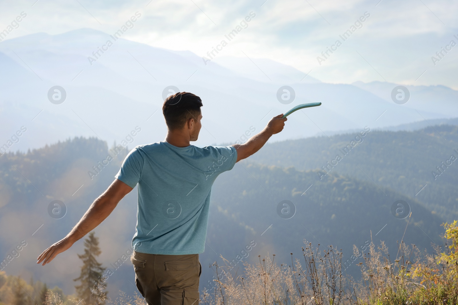 Photo of Man throwing boomerang in mountains on sunny day, back view