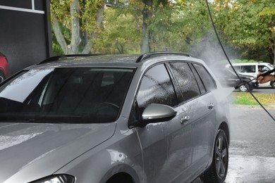 Photo of Man washing auto with high pressure water jet at outdoor car wash, closeup