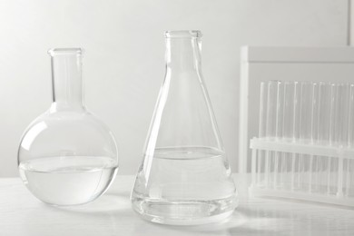 Photo of Laboratory glassware with transparent liquid on white wooden table