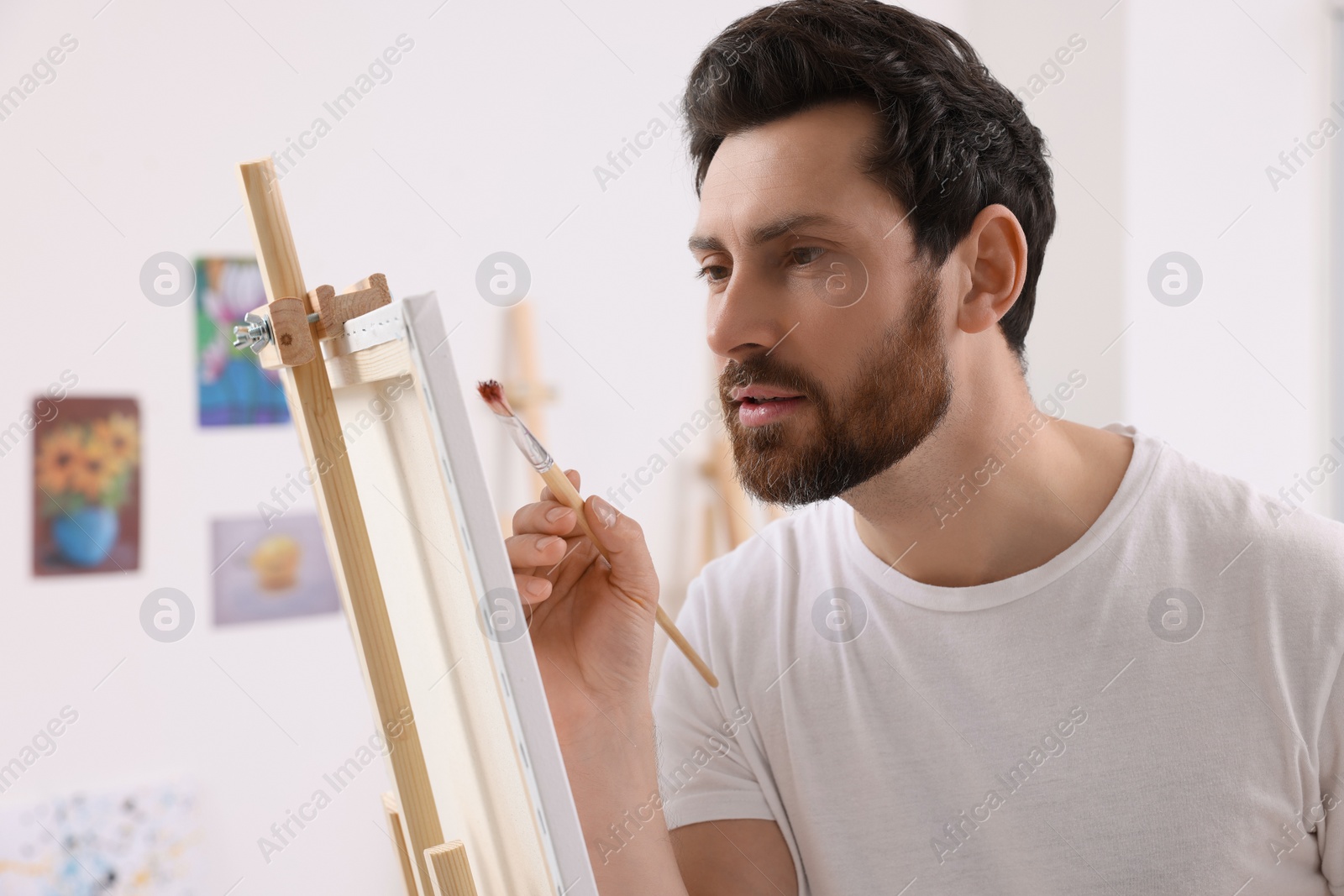 Photo of Man painting in studio. Using easel to hold canvas