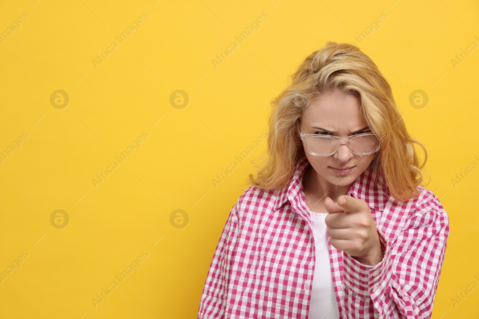 Photo of Aggressive young woman pointing on yellow background. Space for text