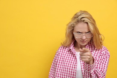 Photo of Aggressive young woman pointing on yellow background. Space for text