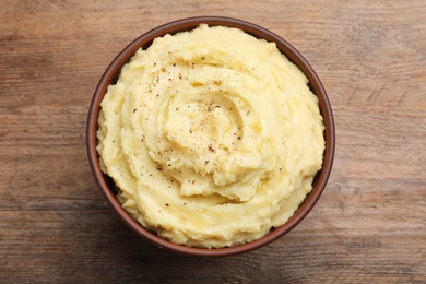 Photo of Bowl of tasty mashed potatoes with black pepper on wooden table, top view