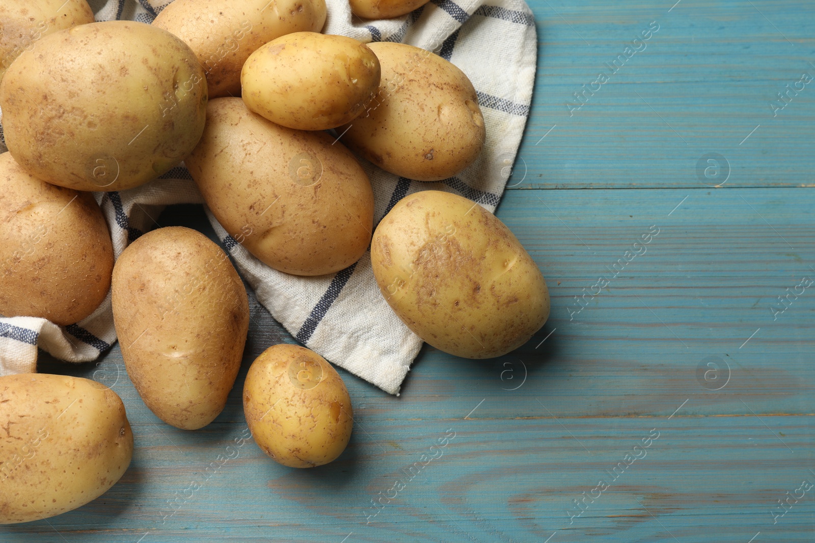 Photo of Raw fresh potatoes and napkin on light blue wooden table, top view. Space for text