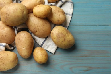 Photo of Raw fresh potatoes and napkin on light blue wooden table, top view. Space for text