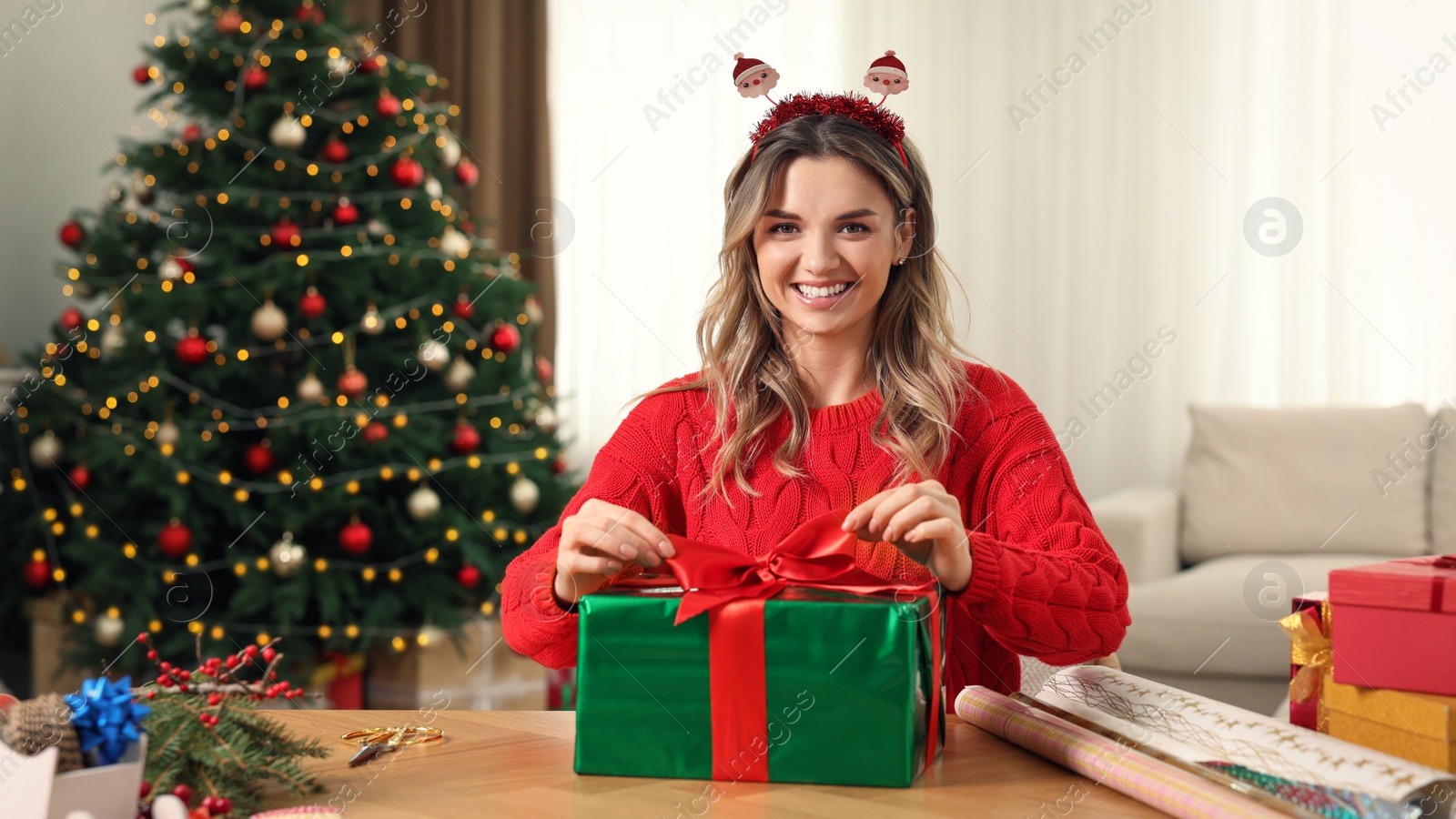 Photo of Beautiful young woman wrapping Christmas gift at home