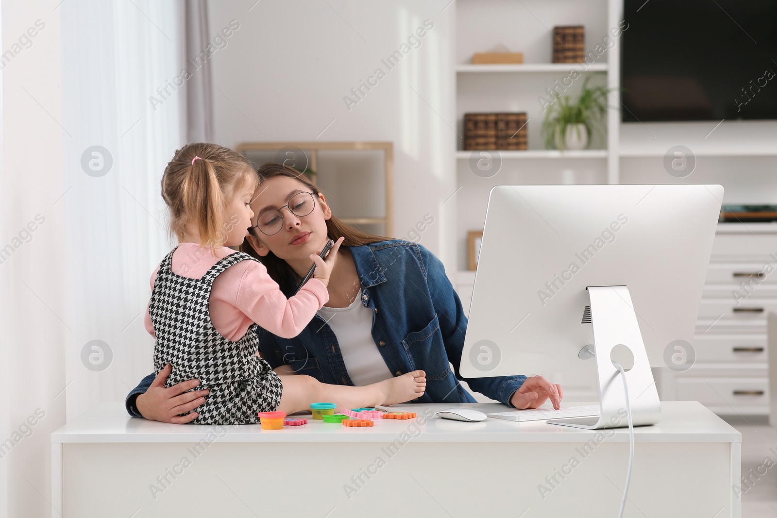 Photo of Mother spending time with her daughter at home. Child sitting on desk. Taking break in remote work