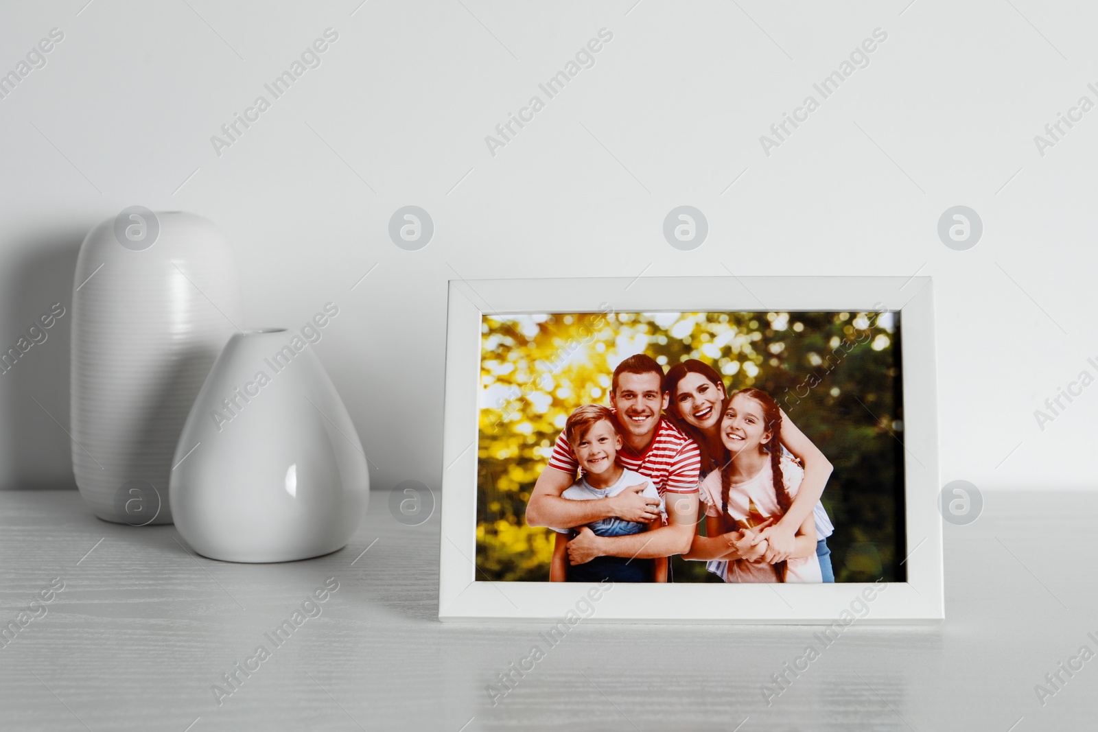 Photo of Frame with family photo and vases on white wooden table indoors