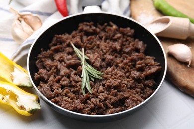 Photo of Fried ground meat in frying pan and products on white tiled table, closeup
