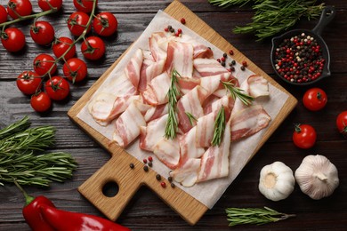 Slices of raw bacon and fresh products on wooden table, flat lay