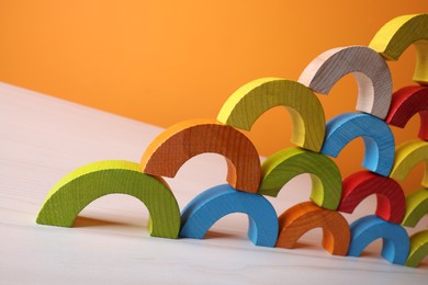 Photo of Colorful wooden pieces of educational toy on light table against orange wall, closeup and space for text. Motor skills development