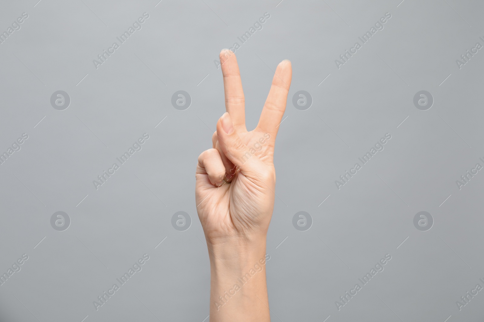 Photo of Woman showing number two on grey background, closeup. Sign language