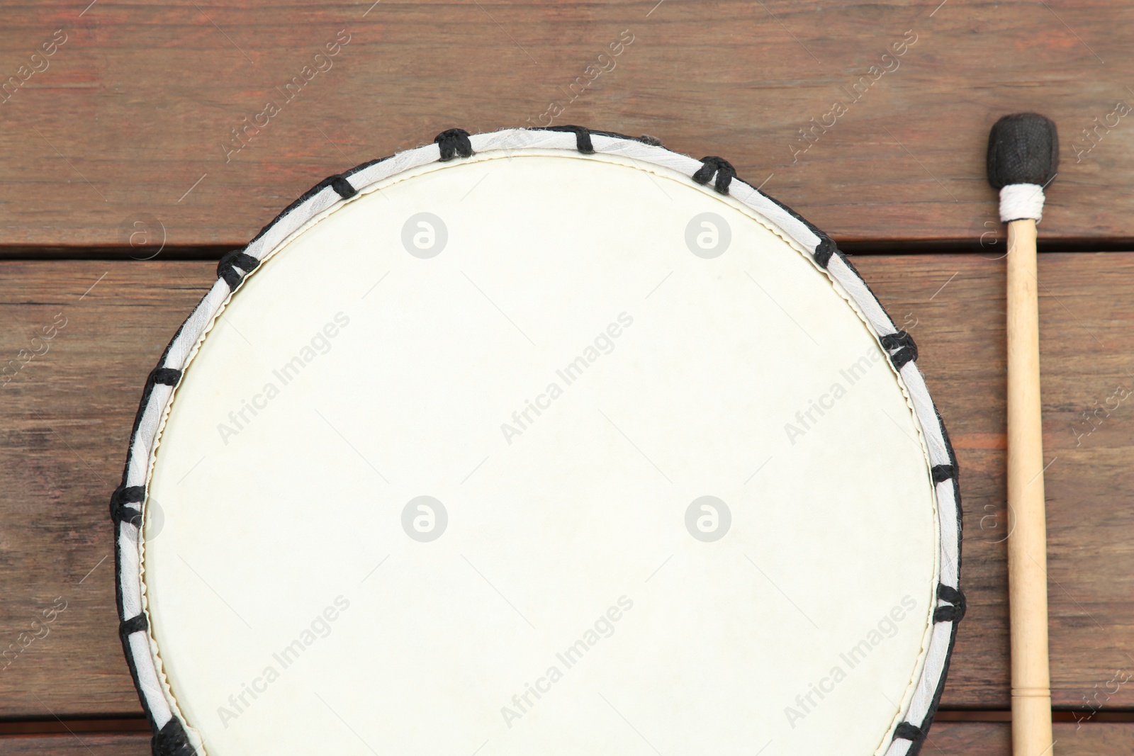 Photo of Modern drum with drumstick on wooden table, flat lay. Percussion musical instrument
