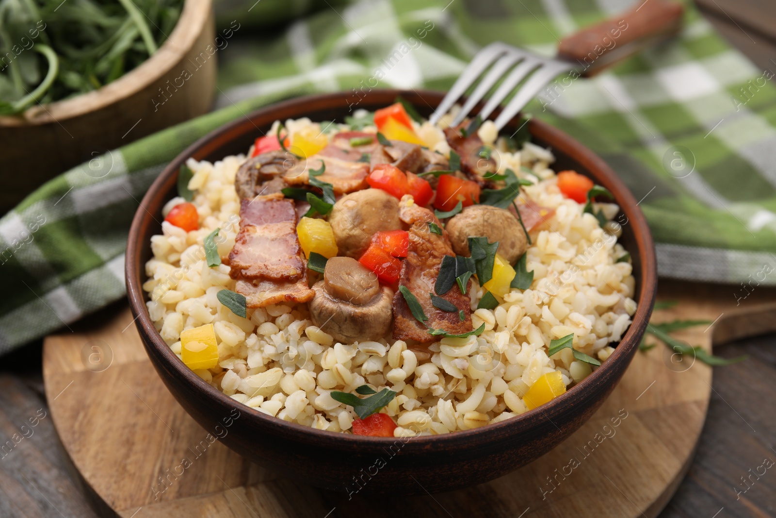 Photo of Cooked bulgur with vegetables, fried bacon and mushrooms in bowl on wooden table, closeup