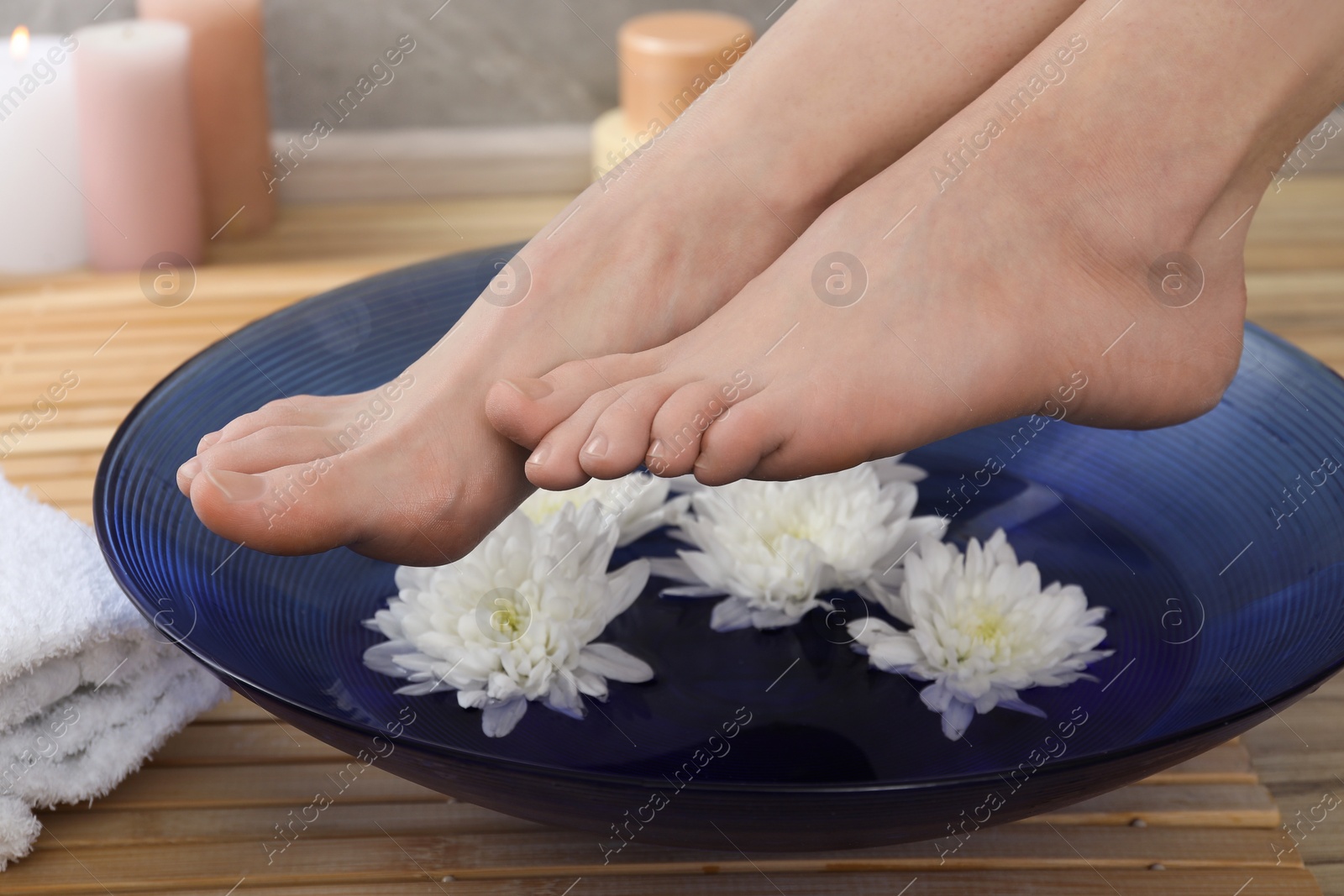 Photo of Woman holding her feet over bowl with water and flowers on floor, closeup. Spa treatment