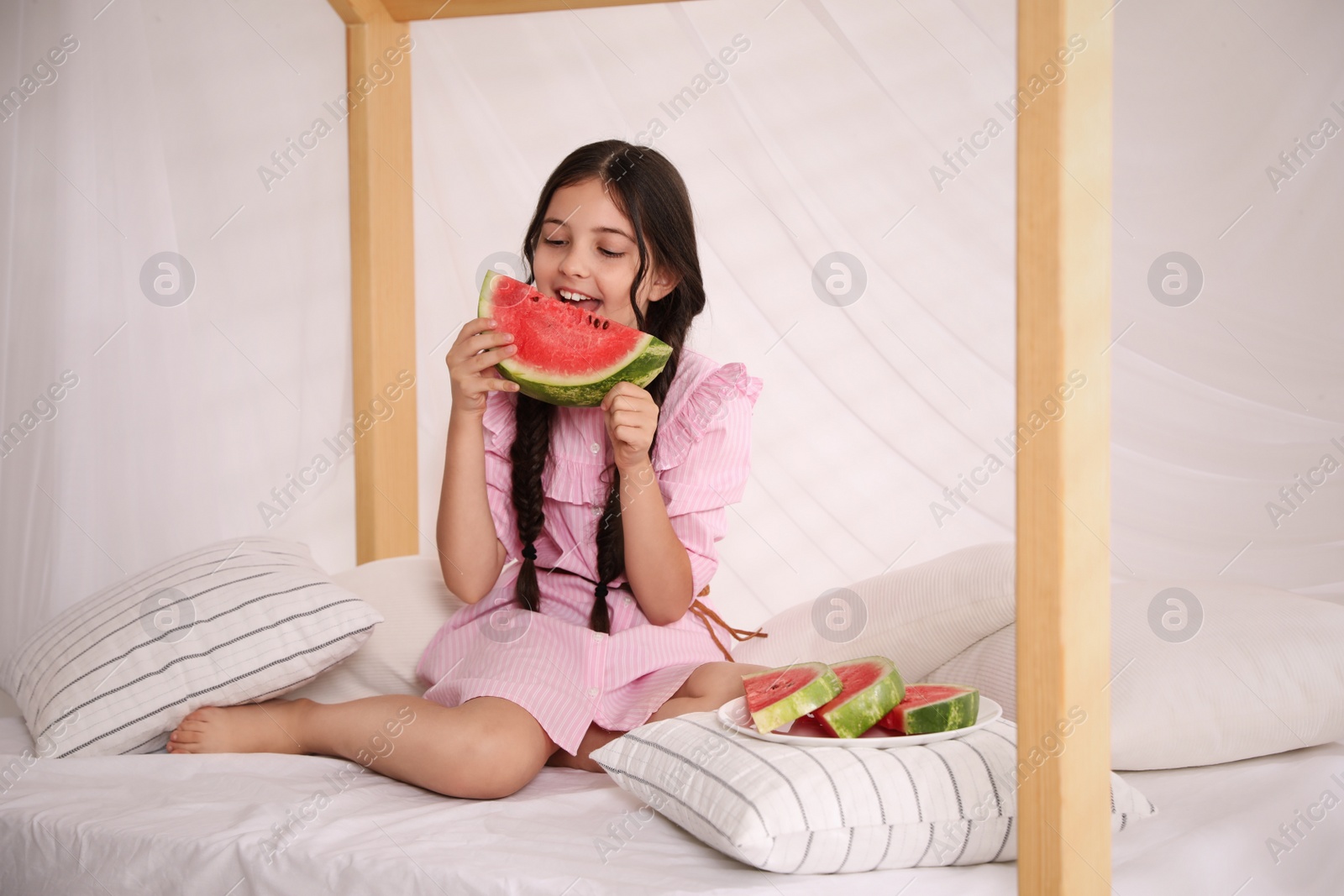 Photo of Cute little girl with watermelon on bed at home