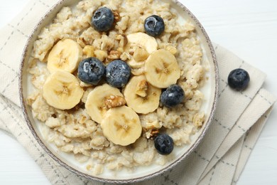 Tasty oatmeal with banana, blueberries, walnuts and honey served in bowl on white wooden table, top view